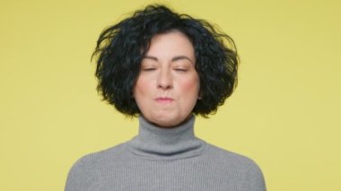 40 'lı yaşlarda kameraya sakız çiğneyen kısa kıvırcık saçlı, neşeli olgun bir kadın. Stüdyoda pastel sarısı arka planda. Kopyalama alanı olan şeker kabarcığı konsepti, yavaş çekim