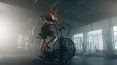 Young female athlete with pink-colored hair toning muscles on upper and lower body. Active woman working out on elliptical machine. High quality 4k footage