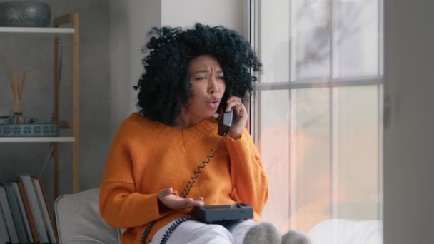 一个有着非洲式发型的心烦意乱的女孩生气了 整理好东西 挂断了电话 身穿橙色毛衣的非洲裔美国女人坐在窗前 手机在电话中对男朋友咒骂的画像 — 图库视频影像