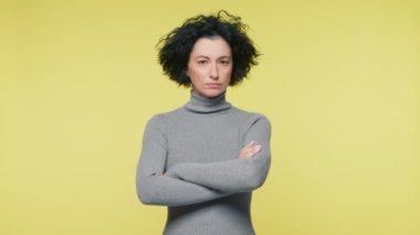 Mature woman 40s crossing arms on plain yellow studio. Beautiful Woman Executive Standing on copy space background slow motion. Portrait Businesswoman Entrepreneur stare evaluating and incredulously