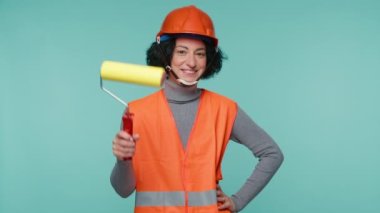 Beautiful Mature woman showing paint roller on blue background. Professional painter worker ready to paint the Wall with Roller. Happy woman 40s having Fun at work. Renovations at Home, construction 