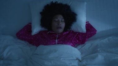 Top view african american woman face with closed eyes bothered by annoying mosquitoes at night while sleeping, black woman slapping herself at cheek to kill gnat in comfortable bed on white linens 4K