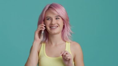 Pretty young attractive woman with pastel pink hair talking on phone with friends, smiling laughing teeth brackets. Indoor portrait girl student makes online order on smartphone, satisfied customer 4K