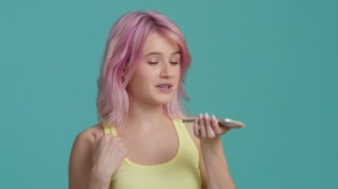 Smiling young woman with pink hair answering by audio message in social network to friend or waiting for the customer support assistance. Happy millennial girl activating smartphone virtual assistant
