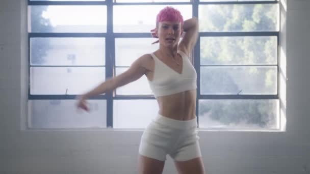 在一个舞蹈工作室的视频制作过程中 活跃而性感的专业舞蹈女 有着粉色的短发 表演嘻哈舞组合 背光穿过大窗 4K镜头 — 图库视频影像