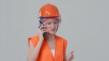 Young architect designer phone call regarding construction site on studio background with copy space for construction. Contractor in working uniform and hardhat controlling working process