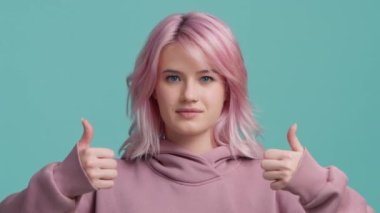 Young hipster girl with pastel pink hair in modern hoodie making good-bad decision isolated teal blue background. Girl make choice, showing decision thumb up or thumb down, like or dislike, yes or no