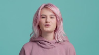 Young fresh creative hipster girl 20s licking plump lips and blowing the air kiss looking straight in camera. Young playful woman face licking sexy lips and flirting. Attractive woman with pink hair