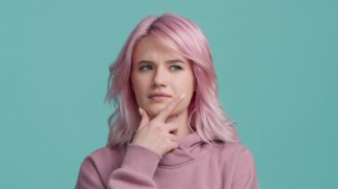 Clever student hipster girl with creative pink hair considering serious plan, solving problem in mind, thinking over smart idea, pondering and musing answer, indoor studio shot isolated on blue wall