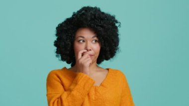 Bewildered confused dark skinned woman with afro hair has doubts and hesitation something. African American girl cant make right decision poses against blue background. Confused Afro American girl 4K