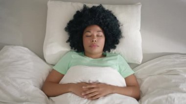 Beautiful African American woman waking up through a nightmare on early morning in bright sun light. Young female laying in bed sleeping, suddenly woken up by nightmare, screaming and shaking hands 4K