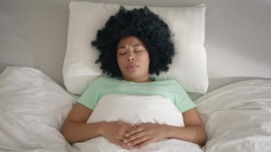 Young female laying in bed sleeping, suddenly woken up by nightmare, screaming with wide opened eyes 4K. Beautiful African American woman waking up through a nightmare on weekday morning in sun light