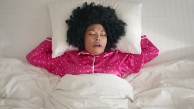 Top view african american woman face with closed eyes bothered by annoying mosquito while sleeping on early morning. Black woman slapping herself at cheek to kill gnat in comfortable white bed linens