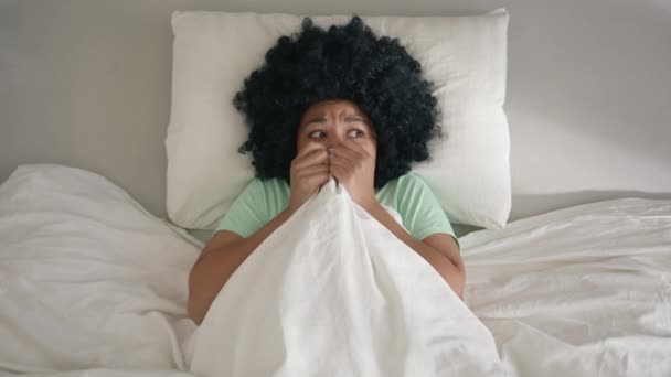 アフリカ系アメリカ人の成人女性は朝 自宅やホテルの部屋で騒音におびえていた 毛布の下にアフロの毛のインフィニティを持つ女の子 モンスターやゴーストスローモーション悪夢を見るために怖がって周りを見て — ストック動画