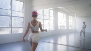 Young beautiful girl with pink hair moving body enjoying practice looking at mirror reflection. People and leisure activities concept 4K. Alone dancer woman dancing hip-hop in urban dancehall indoors