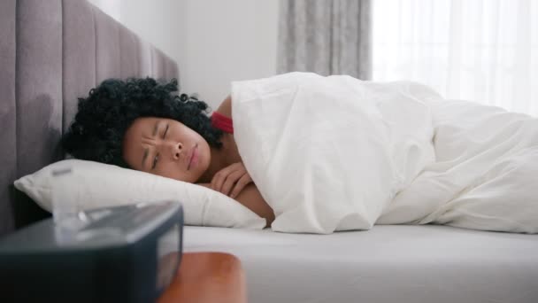 眠い黒の女の子は毛布でカバーし 遅い動きを眠り続ける アフリカ系アメリカ人女性のベッドで寝ることは ベッドサイドテーブルの上に聞こえる活性化されたデジタル目覚まし時計を無効にするために早起き — ストック動画
