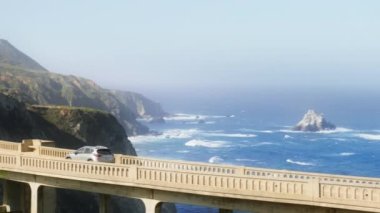 Cinematic following shot of SUV car driving by world famous Bixby bridge 4K shot on RED camera. Road trip concept footage copy space for scenic travel. West Coast tourism on vacation in California USA