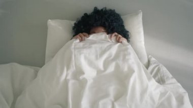 Playful woman of color laughing and having fun in bedroom. Making kissy face and looking cross eyed. Goofy young african american girl making funny faces, being silly while lying in bed under blanket