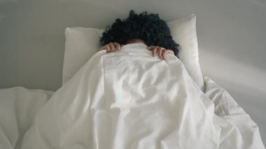 Top view close up woman of color with dark curly hair surprisingly open mouth on sunny morning 4K slow motion. Happy playful African American woman peeking out from blanket in bed, smiling to camera