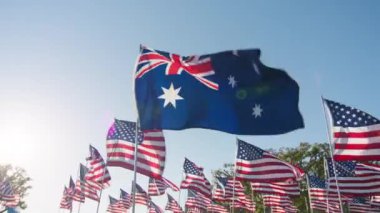 Flag of Australia waving wind with many American flags on motion background, golden sunset hour with sun flare. National Australian flag visualizing independence, freedom, economy partnership business