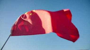 Red flag of China waving wind with clear blue sky on motion background, golden sunset hour with sun flare. National Chinese flag visualizing independence, freedom, economy partnership business