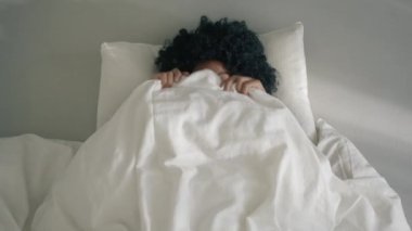 Closeup cheerful woman of color making funny face expressions in bed. Positive funny girl with afro hair fooling around at camera. Portrait joyful lady having fun bedroom. Happy model making grimaces