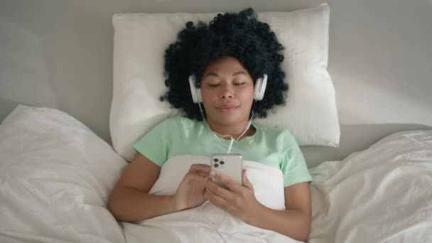 モバイルアプリケーションからお気に入りの音楽リストを楽しみ 晴れた朝に寝室の快適なベッドで一人でリラックス4K — ストック動画