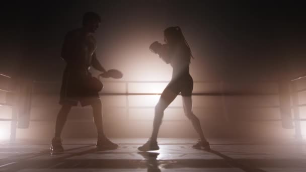 女性キックボクサーと屋内で働く認知されていないコーチ 彼女の体の筋肉や持久力を訓練する女性のクローズアップビュー 高品質4K映像でゴールデンセピアブロンズ霧バックライト — ストック動画