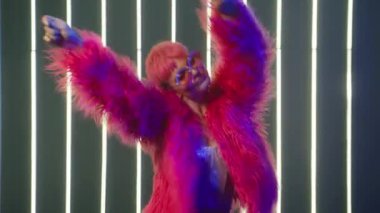 Girl dancer dancing at night club. Young girl with short pink hair moves rhythmically. Pretty Dancer with confident sexy face expressions dancing in fancy pink fur coat and rainbow sunglasses slow mo