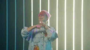 Funny hipster woman dancing at light wall dance studio club. Funky girl in pink glasses and fashionable denim jacket at dance party enjoying crazy celebration, generation z performing fun dance moves