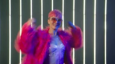 Young Girl with bright pink hair raising and waving arms in dancing moves. People Energy celebrating New Year Slow Motion. Happy Laughter Trendy Female Listen Music and Dance in Night club neon lights