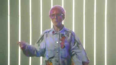 Active energetic confident hipster woman dance in studio with creative neon light wall on background. RED camera shot of young expressive woman with pink glasses and beanie hat performing vogue dance
