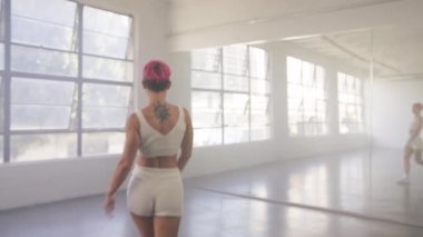 Alone dancer woman dancing hip-hop in urban dancehall indoors. Young beautiful girl with pink hair moving body enjoying practice looking at mirror reflection. People and leisure activities concept 4K
