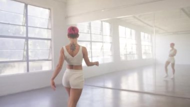 Young beautiful girl with pink hair moving body enjoying practice looking at mirror reflection. People and leisure activities concept 4K. Alone dancer woman dancing hip-hop in urban dancehall indoors
