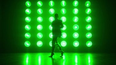 Beautiful sexy woman in oversized blazer and shiny boots performing sensual dance. Silhouette of gorgeous girl dancing in nightclub, performing sensual movements illuminated green lamps. Nightlife
