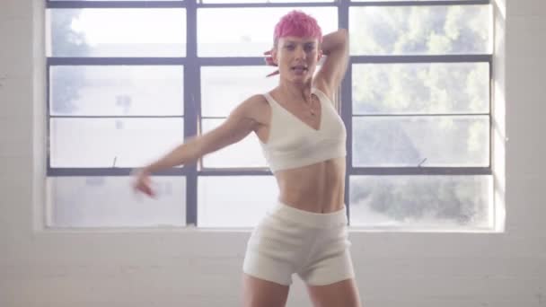 在一个舞蹈工作室的视频制作过程中 活跃而性感的专业舞蹈女 有着粉色的短发 表演嘻哈舞组合 背光穿过大窗 4K镜头 — 图库视频影像