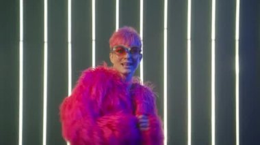 Cinematic footage of young funny woman doing activities in bright hot pink magenta color fluffy fur coat on neon lights background in night club. Silly girl having fun and dancing funny disco moves