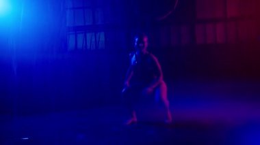 Hot girl dancing under pouring rain water. Dancer with wet body with real strobe lights in colorful light urban garage grunge studio. Sexy body posing in futuristic background. Erotic show slow motion