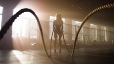 Close-up view of sporty woman performing battle ropes exercises indoors. Workout inspiration motion wallpaper with active, sporty girl. High quality 4k footage
