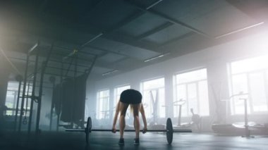 Young, caucasian sportswoman exercising to target large muscle groups and help strengthen body. Back view of unrecognizable, strong woman lifting weights with a barbell. High quality 4k footage