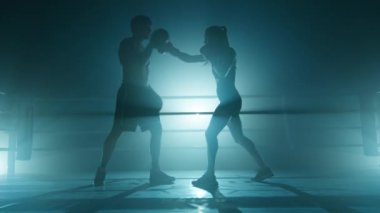 Spor salonunda bir kadını eğiten bir adamın yakın çekimi. Tanınmayan koç içeride bayan kickboksörle antrenman yapıyor. Soğuk mavi sisli arka planda yüksek kalite 4K görüntü.