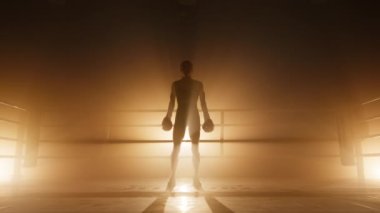 Genç bayan kickboksör karanlıkta tek başına çalışıyor. Tanınmayan kızın atlayıp vücut kaslarını ısıttığı yakın plan. Altın turuncu bronz sisli arka ışıklandırmalı 4K 'lık yüksek kaliteli görüntü.