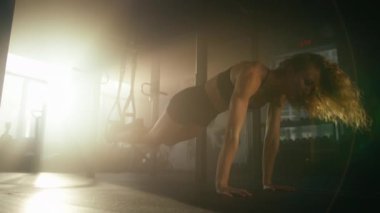 Young, blonde-haired athlete using straps and gravity for intensive workout. Close-up view of healthy, active woman training her abs muscles in modern gym studio. High quality 4k footage
