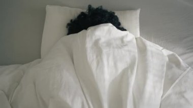 Woman of color looking at bright sun and closing eyes, hiding under blanket. African American girl waking up in bed on early morning, feeling tired after sleepless night, lack of sleep and laziness