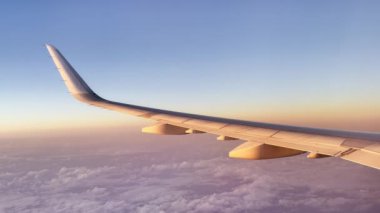 Aerial view of rose golden sunrise or sunset light and clouds seen through airliner window in morning or evening. Aerial view of cloudscape in dawn through plane window. Smooth flight passenger view