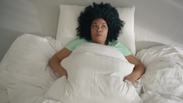 从上往下看 年轻的非洲裔美国女人躺在床上 用大枕头盖住头 遮掩现实 不想看到光明 不想醒来 抑郁症或精神健康问题发作 — 图库视频影像