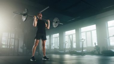 Sportif, genç bir vücut geliştiricinin dolu ağırlık taşıyan bir halteri kaldırışı yakın plan görüntüsü. Siyah spor giyimli aktif sporcu içeride yoğun bir eğitim alıyor. Yüksek kalite 4k görüntü