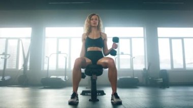 Female athlete performing upper dumbbell workout. Close-up view of caucasian woman promoting muscle growth using weight equipment in modern gym studio. High quality 4k footage