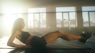 Side view of caucasian, blonde-haired woman training her abs muscles on a soft mat. Portrait of a sporty girl building lean body in bright, sunny gym studio. High quality 4k footage