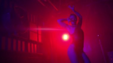 Wet girl performs contemporary dance under water rain on scene in intimate red purple studio light and strobing beam. Modern dance, slow motion in cyberpunk futuristic background in strobe spotlights